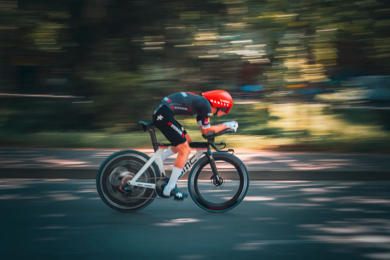 A time-trial cyclist in an aerodynamic tuck on a flat road, illustrating how raw power and aerodynamics — not weight — set speed on the flat.